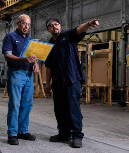 Hayden employees standing in larg industrial facility with documents in hand, pointing and looking off camera